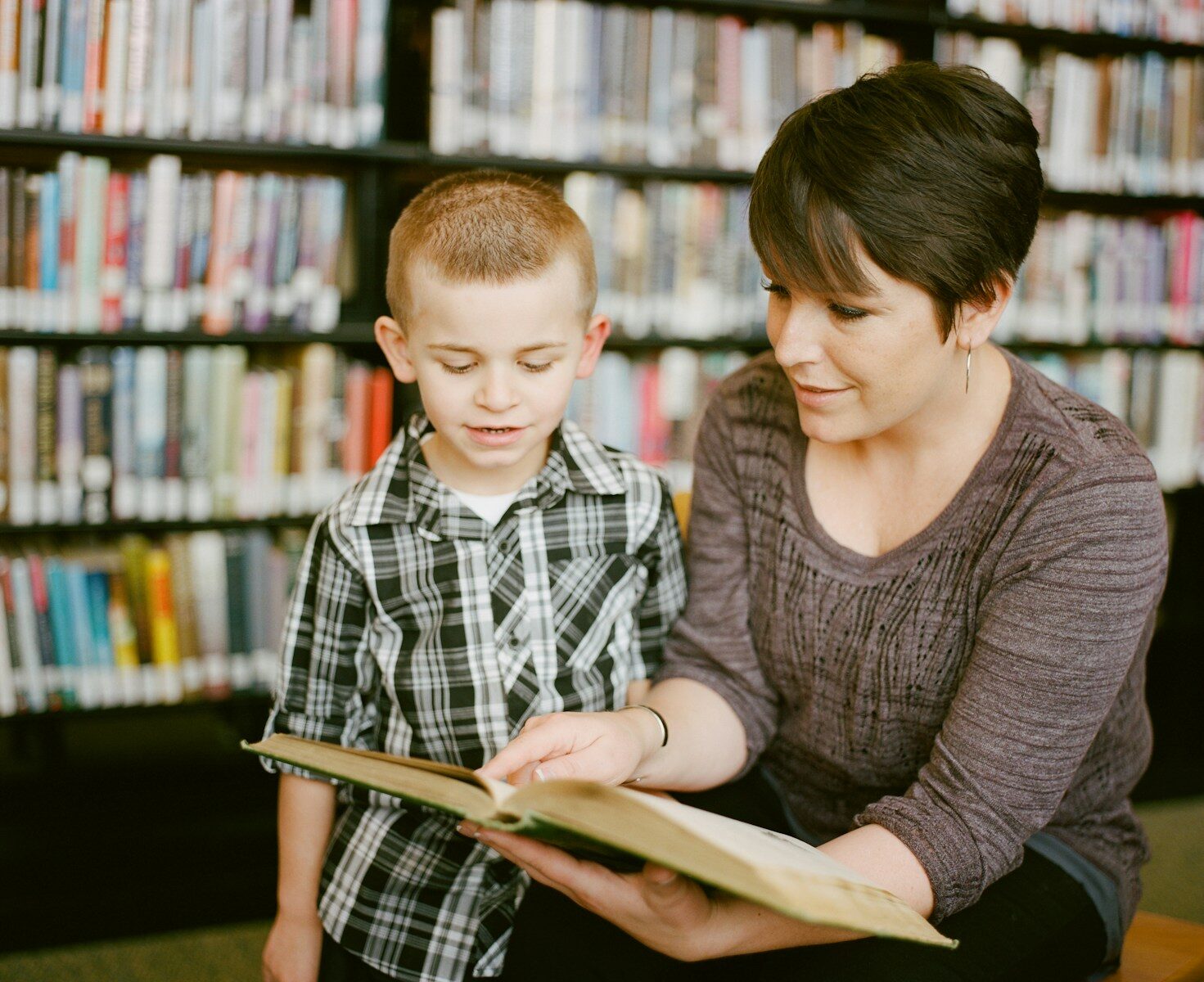 A woman and a child reading a book together in a library
